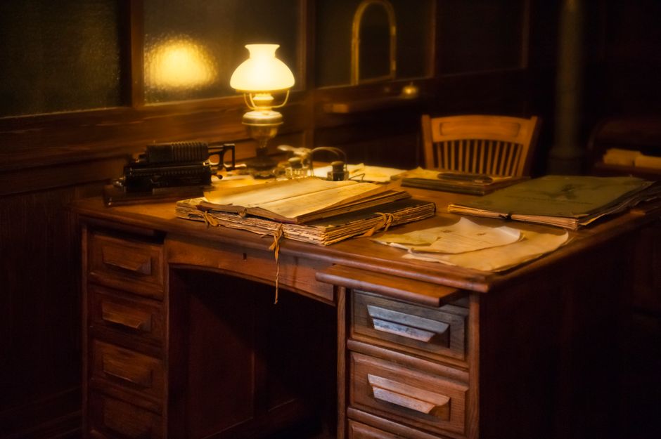 Cozy vintage office setting with an antique typewriter, lamp, and paperwork on a wooden desk.