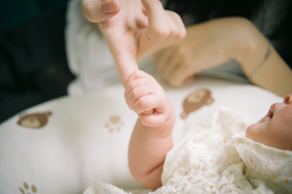 Close-up of a baby holding a parent's finger, symbolizing care and connection.
