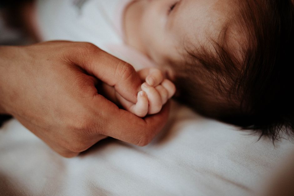 Close-up of a baby's hand gently held by a parent, symbolizing love and care.