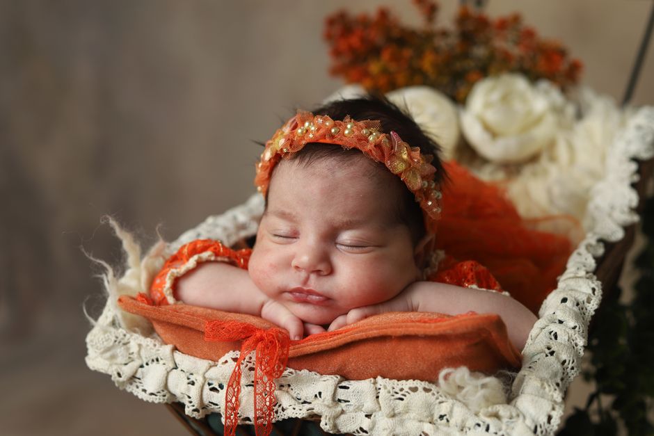 A serene sleeping newborn with floral headband in a cozy setting, captured indoors.