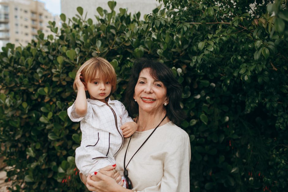 A loving grandmother with her grandchild smiling outdoors in a lush garden setting.