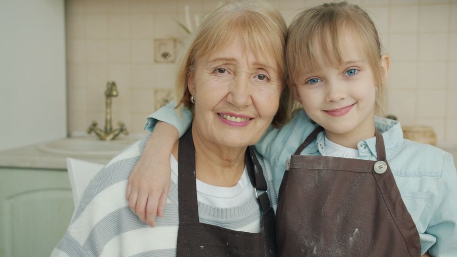 Grandmother and granddaughter smiling in kitchen wearing aprons.