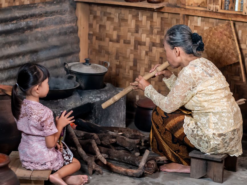 A grandmother and child in a traditional Indonesian kitchen, preparing a meal over a wood fire.