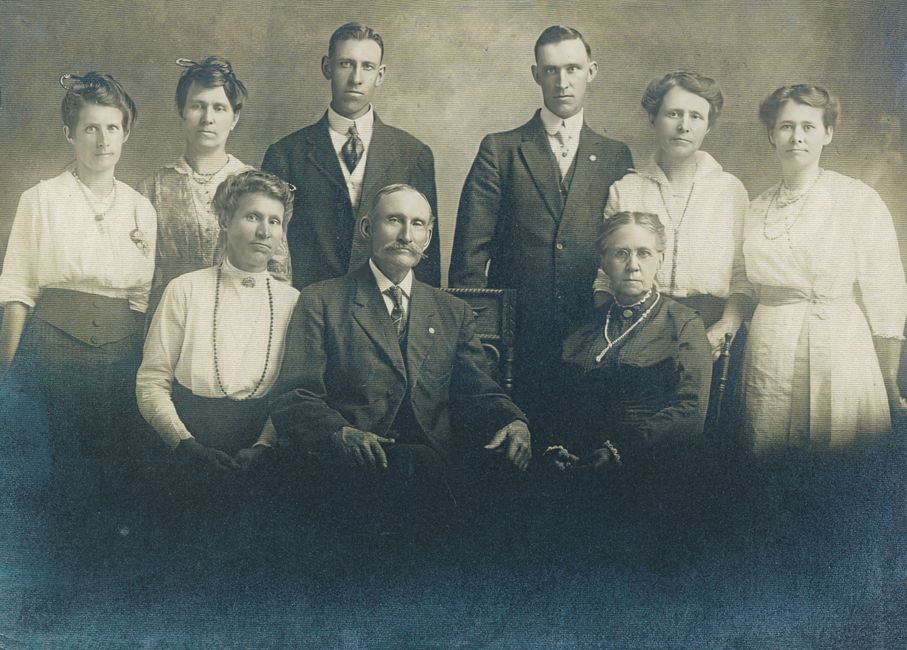 Retro family portrait with seven adults in early 1900s attire.