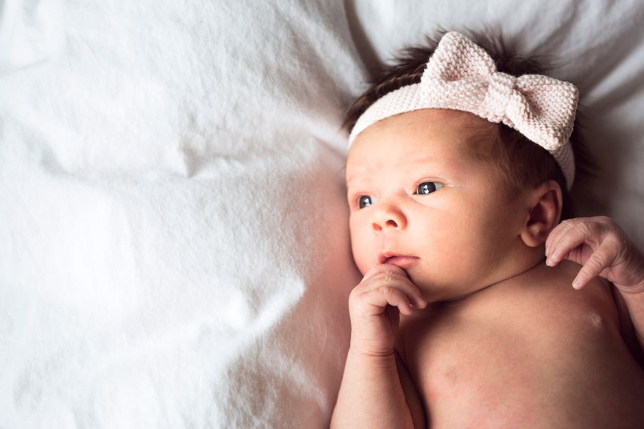 Charming portrait of a newborn baby with a pink bow headband lying on a soft white blanket.