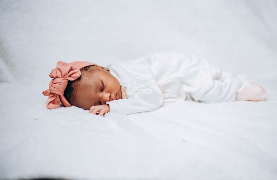 Adorable baby sleeping peacefully on white fabric, wearing a pink headband.
