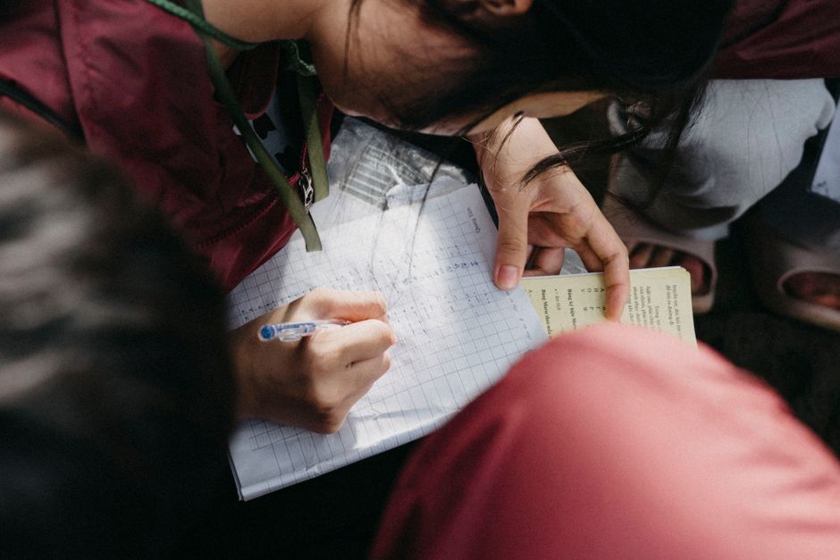 A young person writing in a notebook while attending an outdoor class or study session.